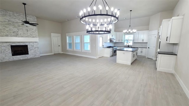 kitchen featuring white cabinetry, stainless steel gas stove, a center island, a stone fireplace, and ceiling fan with notable chandelier