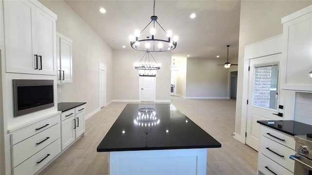 kitchen with ceiling fan with notable chandelier, built in microwave, decorative light fixtures, white cabinetry, and a kitchen island