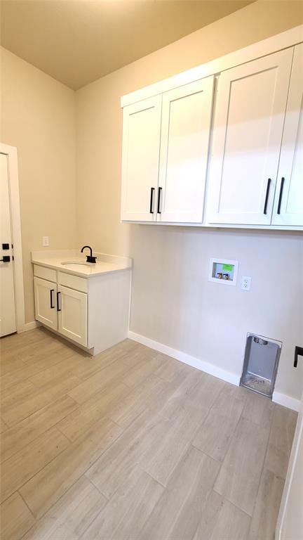 clothes washing area with cabinets, sink, hookup for a washing machine, and light hardwood / wood-style flooring