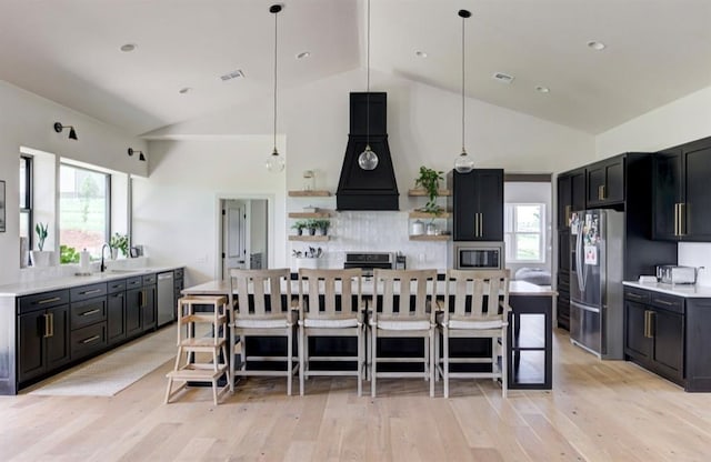 kitchen with a kitchen bar, stainless steel appliances, light hardwood / wood-style floors, and range hood