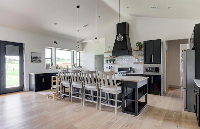 kitchen featuring appliances with stainless steel finishes, custom exhaust hood, high vaulted ceiling, light hardwood / wood-style flooring, and a center island