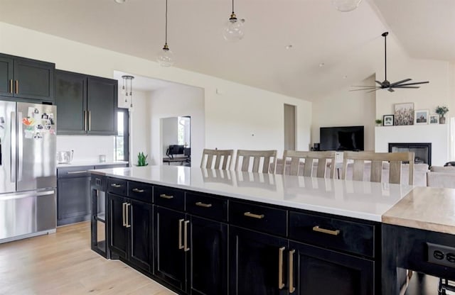 kitchen with vaulted ceiling, decorative light fixtures, light hardwood / wood-style floors, a breakfast bar area, and stainless steel refrigerator