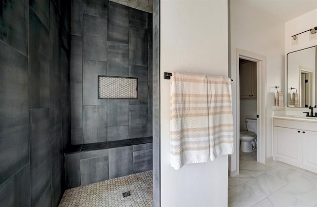 bathroom with a tile shower, vanity, and toilet