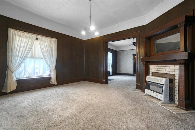 unfurnished living room with heating unit, wood walls, a textured ceiling, light carpet, and a fireplace