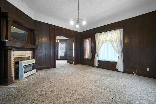 unfurnished living room featuring a textured ceiling, heating unit, light colored carpet, an inviting chandelier, and wood walls