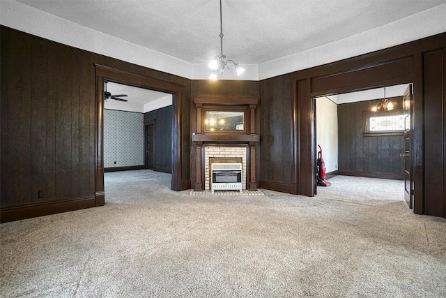 unfurnished living room featuring light carpet, ceiling fan with notable chandelier, wooden walls, a textured ceiling, and a fireplace