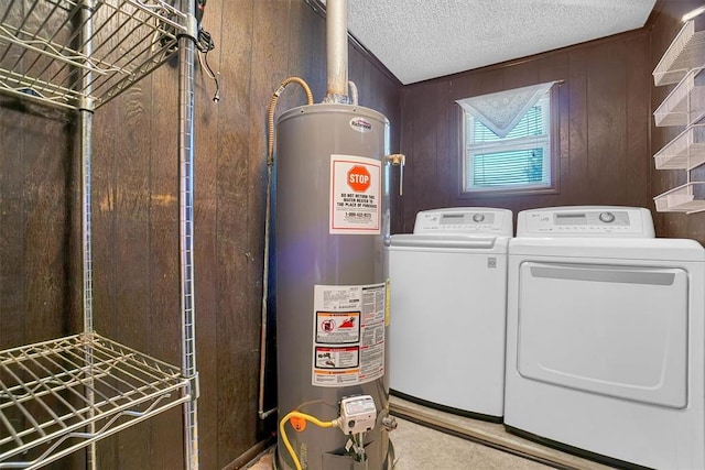 laundry room with washing machine and clothes dryer, a textured ceiling, gas water heater, and wood walls