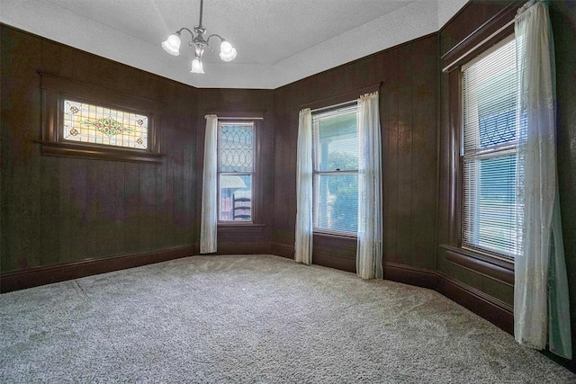 unfurnished room with wood walls, carpet floors, and an inviting chandelier