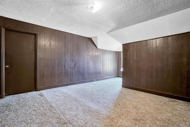 additional living space with wood walls, lofted ceiling, a textured ceiling, and light carpet