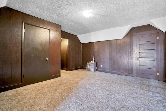 bonus room with a textured ceiling, wooden walls, and lofted ceiling