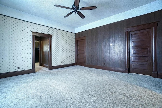 spare room with wooden walls, ceiling fan, light carpet, and a textured ceiling