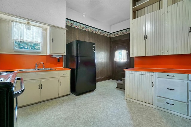 kitchen with black refrigerator, a wealth of natural light, stainless steel range with electric stovetop, and sink