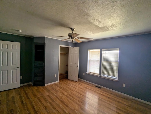 unfurnished bedroom with a textured ceiling, ceiling fan, a spacious closet, hardwood / wood-style floors, and a closet