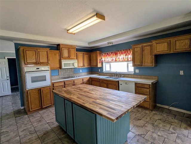 kitchen with white appliances, crown molding, sink, a kitchen island, and butcher block counters