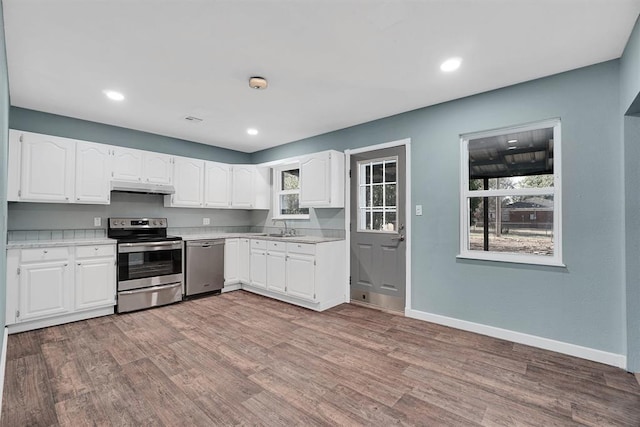 1033 Coe St, Altus, OK 73521 - kitchen featuring appliances with stainless steel finishes, under cabinet range hood, a sink, light countertops, and white cabinetry