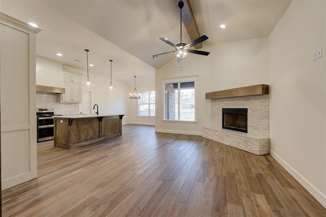 living room with ceiling fan, sink, beam ceiling, hardwood / wood-style flooring, and a stone fireplace