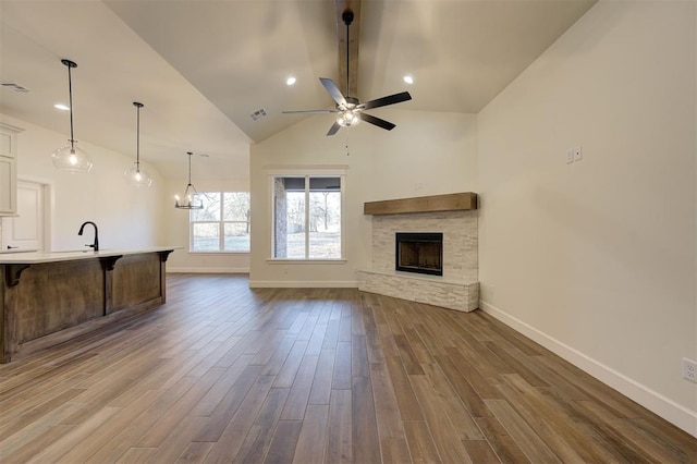 unfurnished living room featuring high vaulted ceiling, a fireplace, dark wood-type flooring, and ceiling fan with notable chandelier