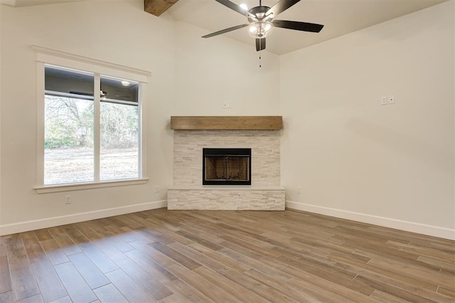 unfurnished living room featuring wood-type flooring, vaulted ceiling with beams, a stone fireplace, and ceiling fan