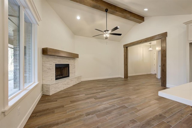 unfurnished living room with vaulted ceiling with beams, hardwood / wood-style flooring, a stone fireplace, and ceiling fan