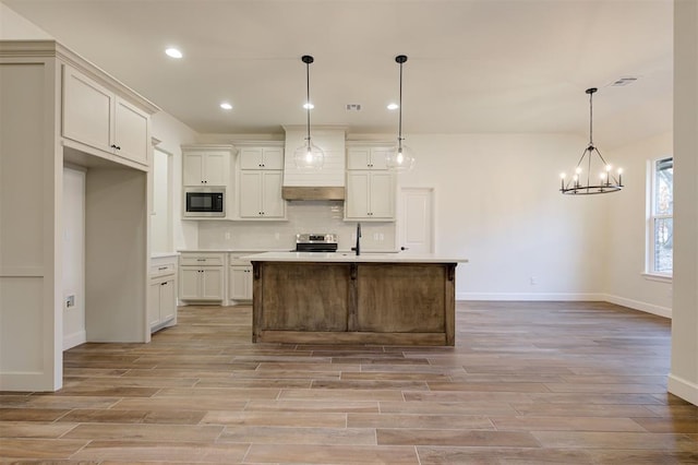 kitchen with hanging light fixtures, an inviting chandelier, light hardwood / wood-style floors, a center island with sink, and appliances with stainless steel finishes