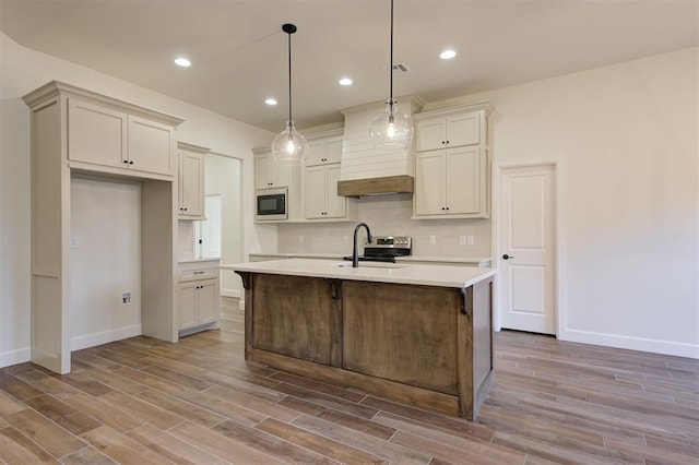 kitchen with hanging light fixtures, tasteful backsplash, hardwood / wood-style floors, a kitchen island with sink, and appliances with stainless steel finishes