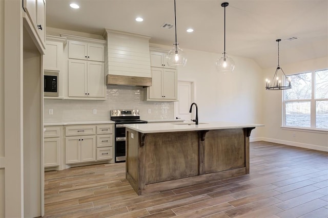 kitchen with a center island with sink, light hardwood / wood-style floors, custom range hood, and stainless steel appliances