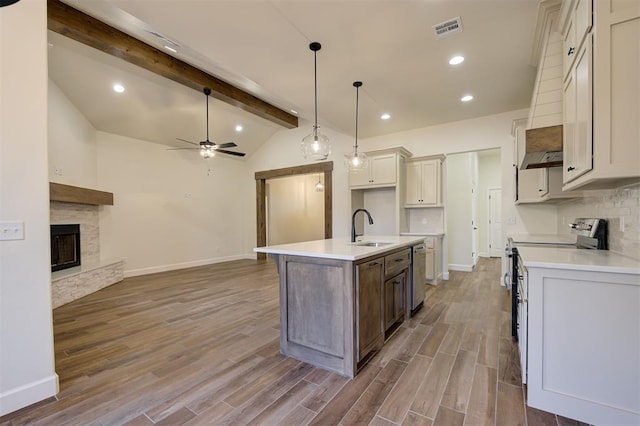 kitchen with stainless steel appliances, ceiling fan, wood-type flooring, lofted ceiling with beams, and a center island with sink