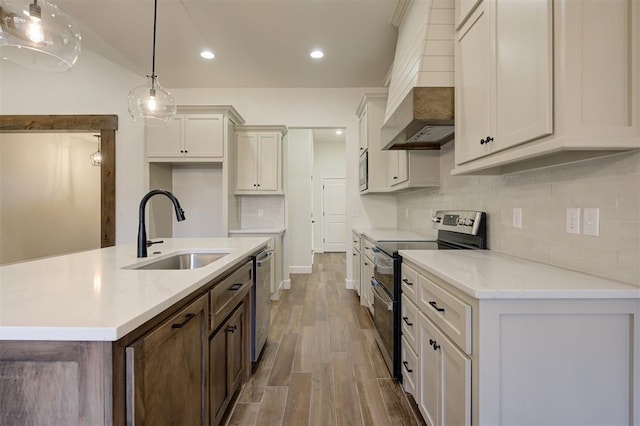 kitchen featuring sink, stainless steel appliances, premium range hood, hardwood / wood-style floors, and decorative light fixtures