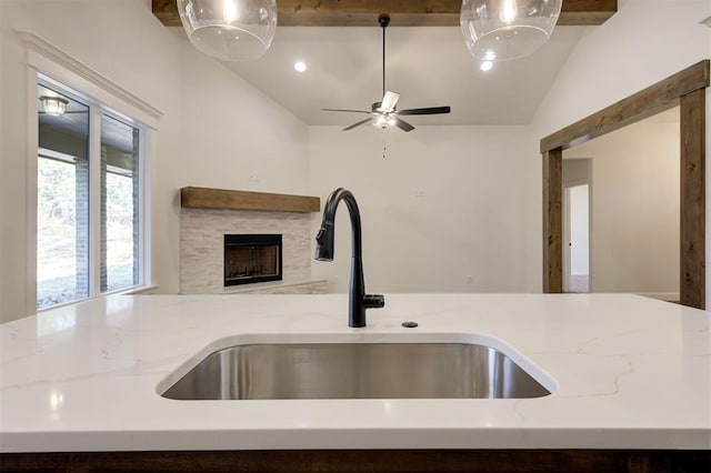 kitchen featuring a fireplace, light stone countertops, sink, and vaulted ceiling