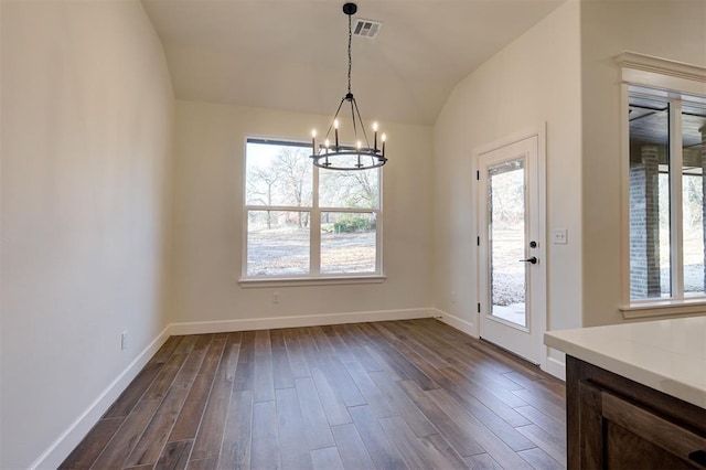 unfurnished dining area featuring a healthy amount of sunlight, lofted ceiling, dark wood-type flooring, and an inviting chandelier