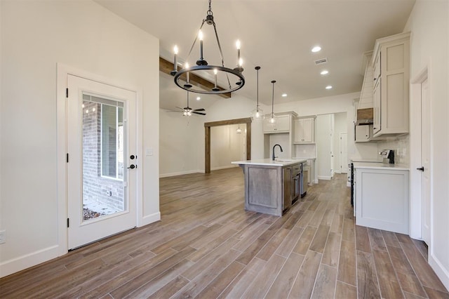 kitchen featuring ceiling fan with notable chandelier, a kitchen island with sink, decorative light fixtures, range, and light hardwood / wood-style floors