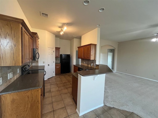 kitchen with tasteful backsplash, kitchen peninsula, black refrigerator, and light tile patterned floors