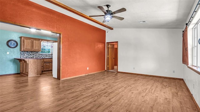 unfurnished living room with a barn door, ceiling fan, light hardwood / wood-style flooring, and lofted ceiling