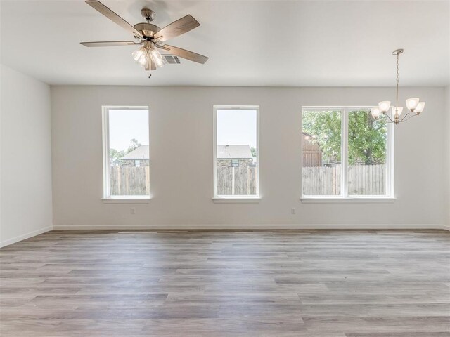 unfurnished room featuring ceiling fan with notable chandelier, a healthy amount of sunlight, and light hardwood / wood-style flooring