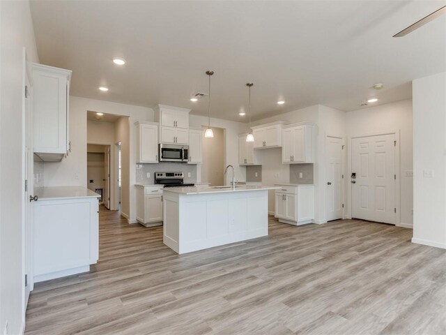 kitchen featuring white cabinets, a center island with sink, hanging light fixtures, appliances with stainless steel finishes, and light hardwood / wood-style floors