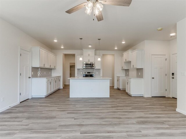 kitchen featuring pendant lighting, white cabinets, light wood-type flooring, appliances with stainless steel finishes, and a kitchen island