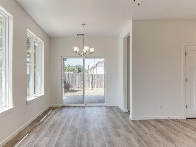 unfurnished dining area featuring a notable chandelier, light hardwood / wood-style floors, and a wealth of natural light