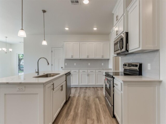 kitchen featuring stainless steel appliances, a kitchen island with sink, sink, decorative light fixtures, and white cabinets