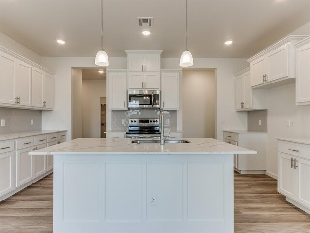 kitchen featuring white cabinets, decorative light fixtures, appliances with stainless steel finishes, and light hardwood / wood-style flooring