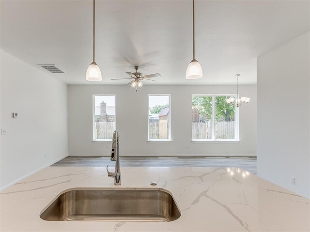 kitchen featuring ceiling fan with notable chandelier, sink, light wood-type flooring, decorative light fixtures, and light stone counters