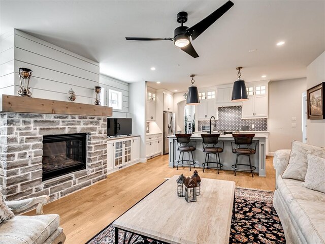 living room with a stone fireplace, ceiling fan, light hardwood / wood-style flooring, and sink