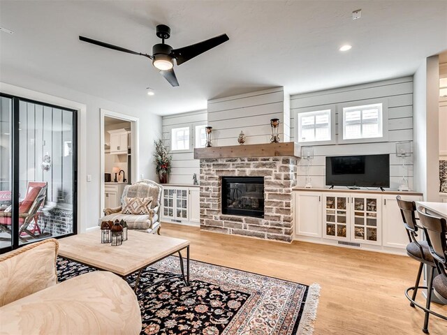 living room with ceiling fan, light hardwood / wood-style floors, and a stone fireplace