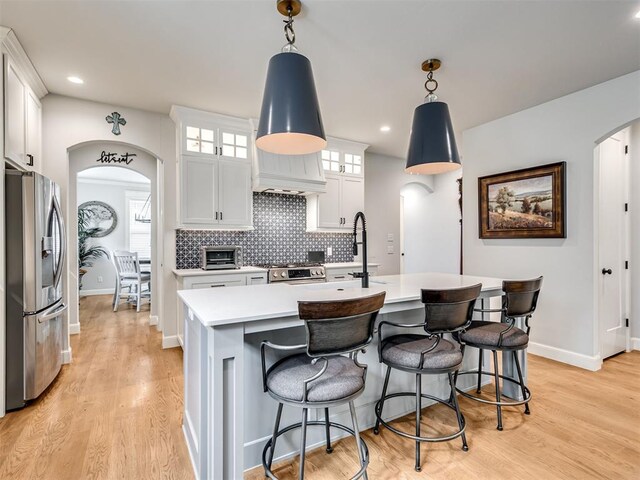 kitchen featuring white cabinetry, stainless steel appliances, an island with sink, pendant lighting, and light hardwood / wood-style floors