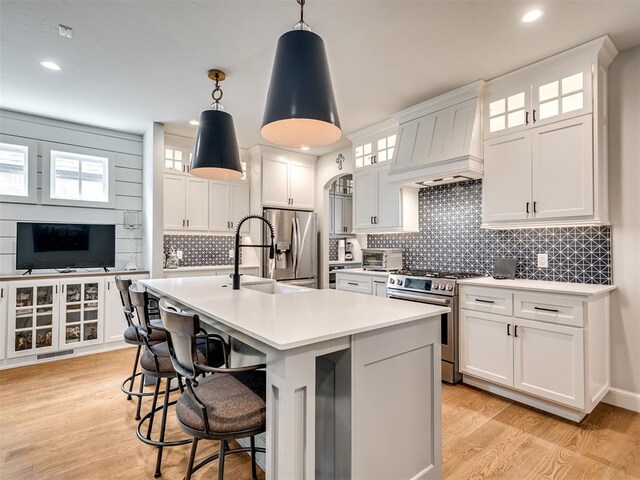 kitchen featuring stainless steel appliances, pendant lighting, a center island with sink, white cabinets, and custom exhaust hood