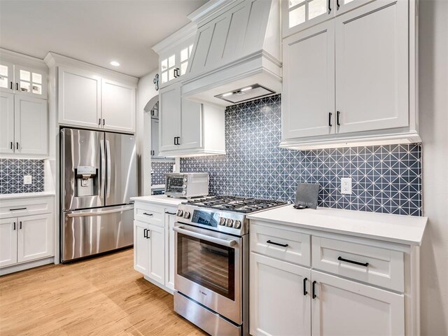 kitchen with custom exhaust hood, decorative backsplash, white cabinetry, and appliances with stainless steel finishes