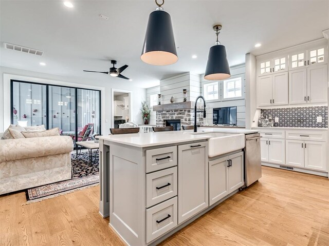 kitchen featuring decorative backsplash, stainless steel dishwasher, pendant lighting, white cabinets, and an island with sink