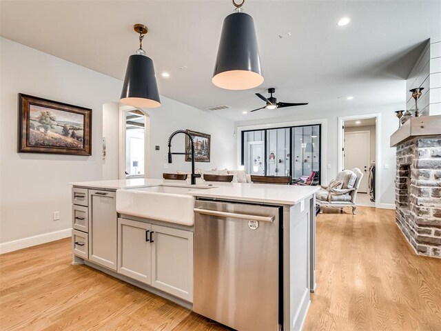 kitchen featuring sink, hanging light fixtures, stainless steel dishwasher, light wood-type flooring, and an island with sink