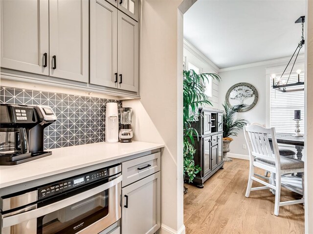 kitchen with an inviting chandelier, pendant lighting, light wood-type flooring, decorative backsplash, and ornamental molding