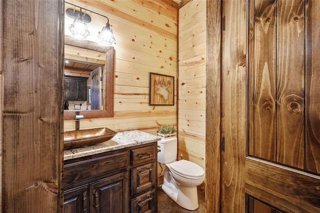 bathroom with vanity, toilet, and wood walls