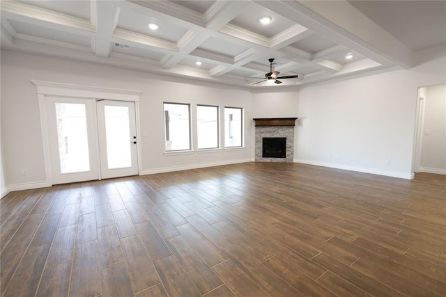 unfurnished living room featuring ceiling fan, a healthy amount of sunlight, a stone fireplace, and dark hardwood / wood-style flooring